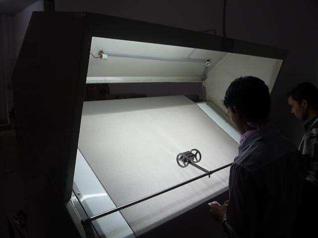 A technician inspecting fabric on a lit inspection machine